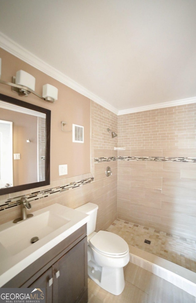 bathroom featuring tiled shower, toilet, tile walls, ornamental molding, and vanity