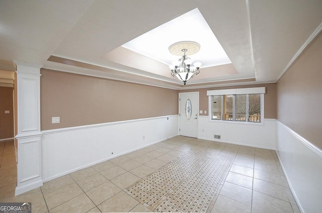 tiled empty room with crown molding, a notable chandelier, a tray ceiling, and ornate columns