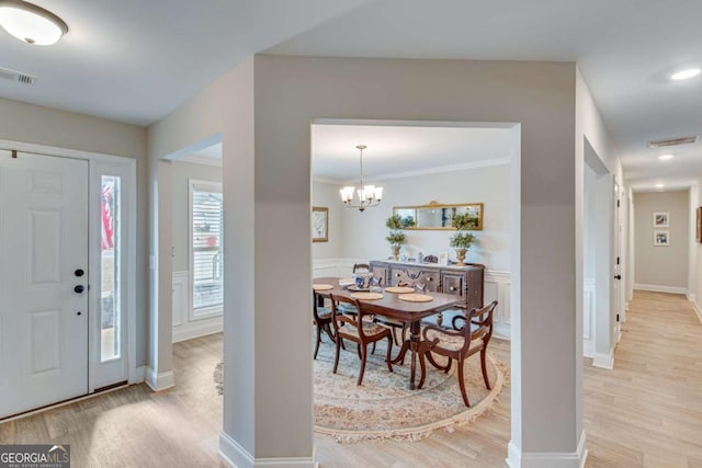 foyer entrance with ornamental molding, a notable chandelier, and light wood-type flooring