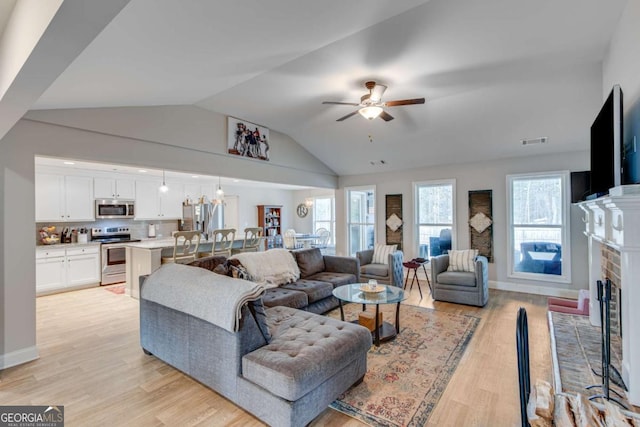 living room featuring vaulted ceiling, a brick fireplace, ceiling fan, and light hardwood / wood-style flooring