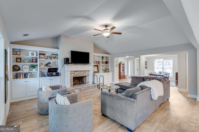 living room with ceiling fan with notable chandelier, lofted ceiling, light hardwood / wood-style flooring, a brick fireplace, and built in shelves