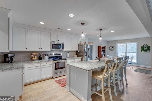 kitchen with appliances with stainless steel finishes, pendant lighting, white cabinets, light stone counters, and a center island with sink