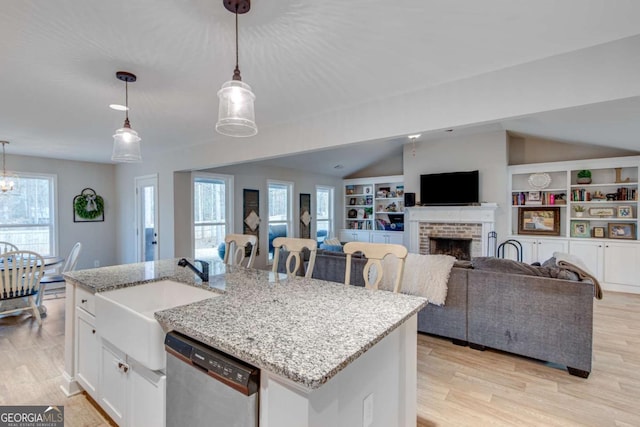 kitchen featuring light stone counters, stainless steel dishwasher, an island with sink, pendant lighting, and white cabinets