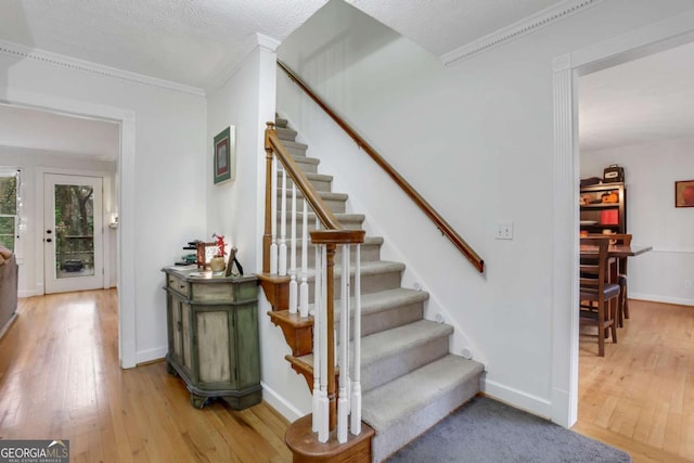 staircase featuring hardwood / wood-style floors, ornamental molding, and a textured ceiling