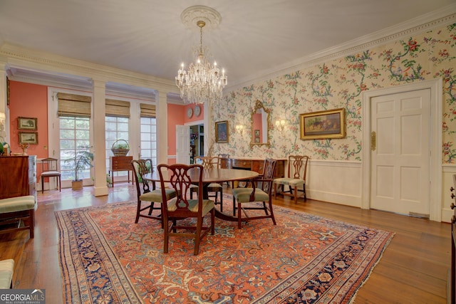 dining space with hardwood / wood-style flooring, crown molding, decorative columns, and a notable chandelier