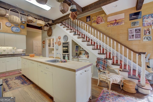 kitchen with sink, light hardwood / wood-style flooring, white cabinetry, a kitchen island, and wood walls