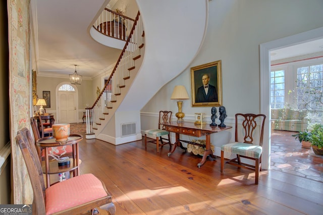 living area with an inviting chandelier, crown molding, wood-type flooring, and a towering ceiling