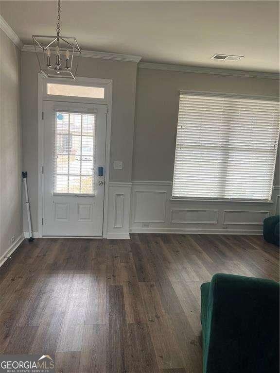 entrance foyer with crown molding, dark wood-type flooring, and a chandelier