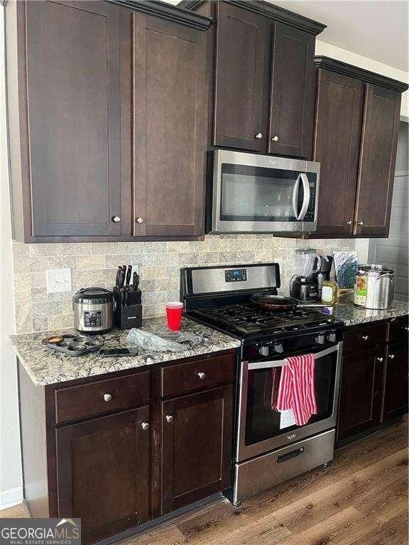 kitchen featuring light stone counters, dark brown cabinetry, appliances with stainless steel finishes, and wood-type flooring