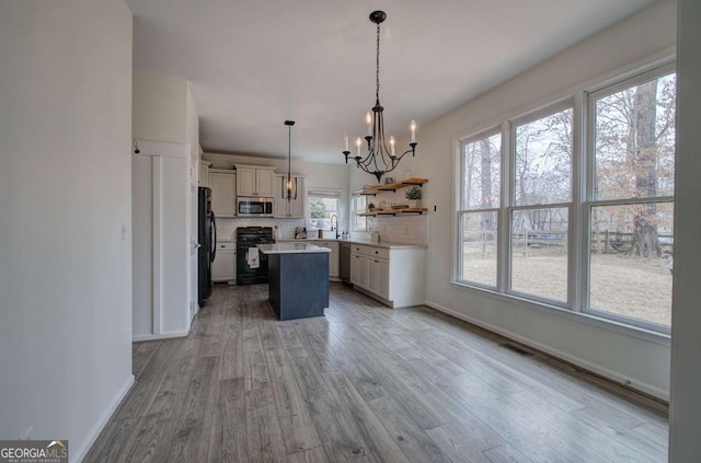 kitchen with black appliances, hanging light fixtures, a kitchen island, decorative backsplash, and white cabinets