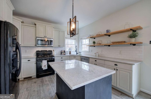 kitchen with sink, decorative light fixtures, light hardwood / wood-style flooring, a kitchen island, and black appliances