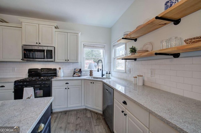 kitchen with appliances with stainless steel finishes, tasteful backsplash, sink, white cabinets, and light wood-type flooring