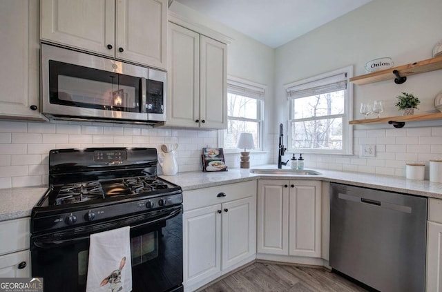 kitchen featuring sink, white cabinets, stainless steel appliances, light stone countertops, and light wood-type flooring