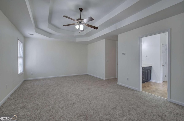 spare room featuring light colored carpet, a raised ceiling, and ceiling fan