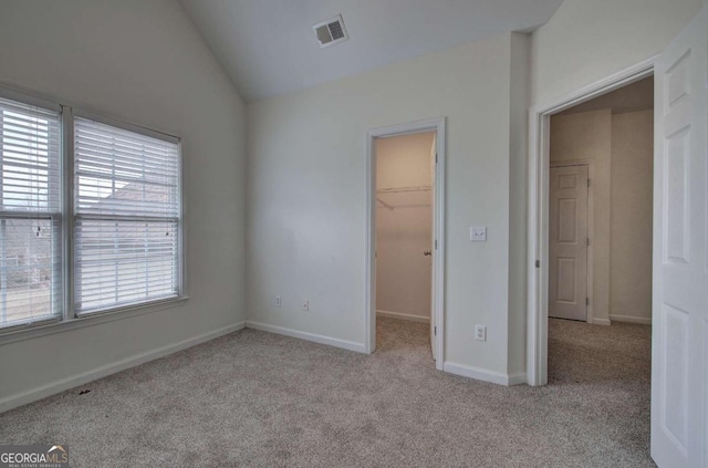 unfurnished bedroom featuring multiple windows, vaulted ceiling, a walk in closet, and a closet