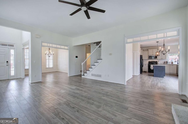 unfurnished living room with hardwood / wood-style flooring, ceiling fan with notable chandelier, and sink