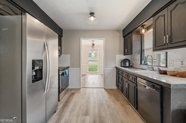 kitchen featuring a wainscoted wall, stainless steel appliances, light countertops, light wood-style flooring, and a sink