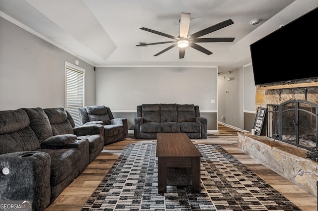 living room with ceiling fan, a fireplace, wood finished floors, baseboards, and a tray ceiling