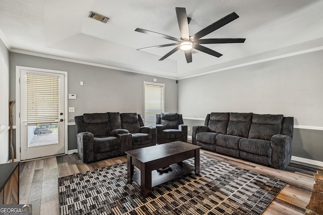 living room with ornamental molding, a tray ceiling, visible vents, and wood finished floors