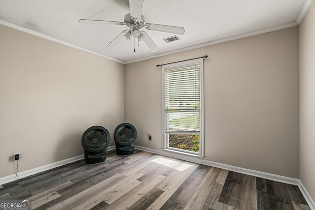 empty room with baseboards, wood finished floors, visible vents, and crown molding