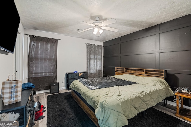 bedroom with a ceiling fan, a decorative wall, a textured ceiling, and wood finished floors