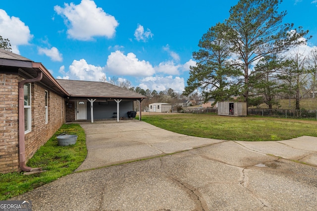 view of property exterior featuring brick siding, a yard, concrete driveway, fence, and an outdoor structure