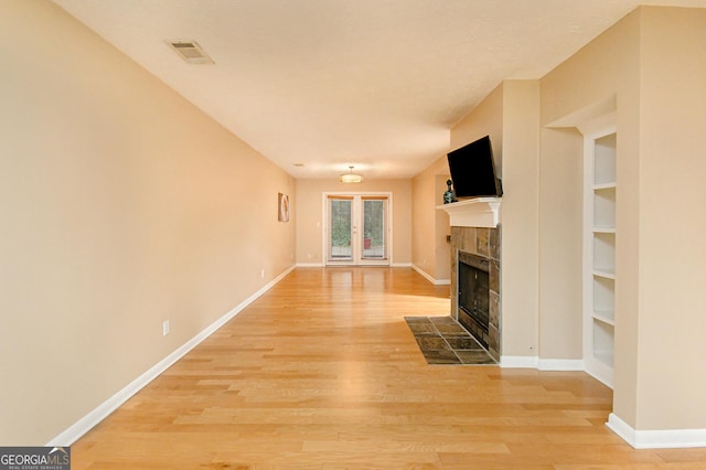 unfurnished living room featuring a tiled fireplace, built in shelves, and light wood-type flooring