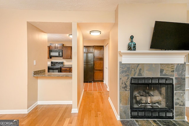 kitchen featuring a tile fireplace, light hardwood / wood-style flooring, and black appliances