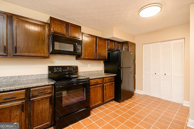 kitchen featuring light stone countertops, light tile patterned floors, a textured ceiling, and black appliances