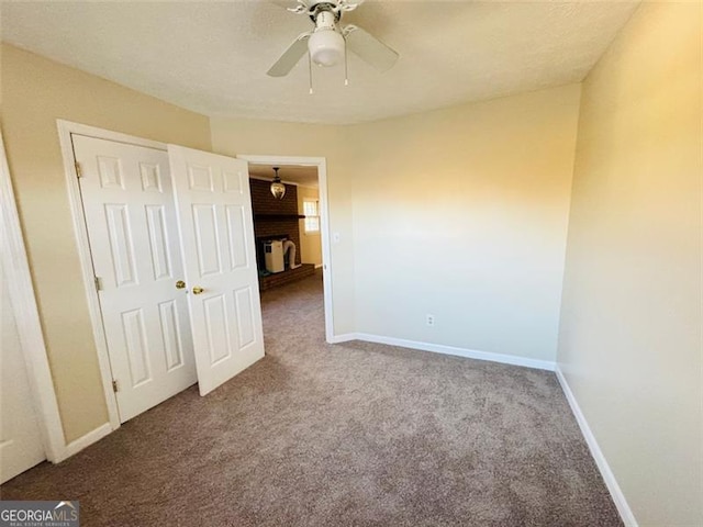 unfurnished bedroom featuring ceiling fan, a fireplace, carpet floors, and a closet