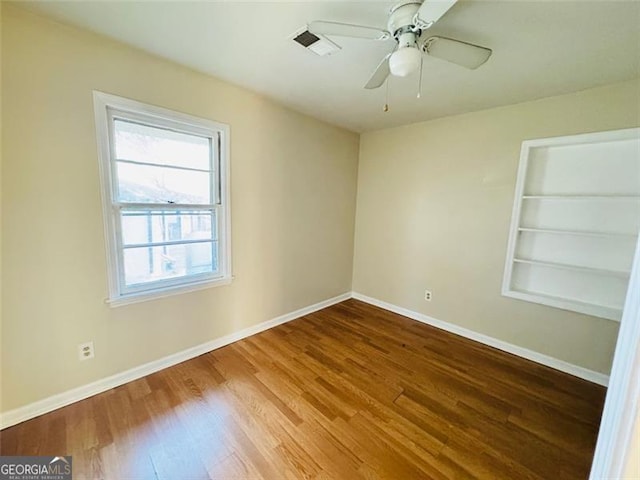 unfurnished room featuring wood-type flooring, built in features, and ceiling fan