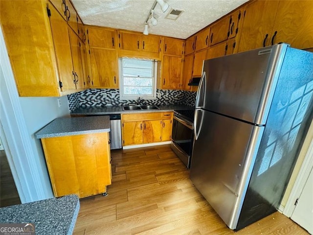 kitchen with sink, stainless steel appliances, light hardwood / wood-style floors, a textured ceiling, and decorative backsplash