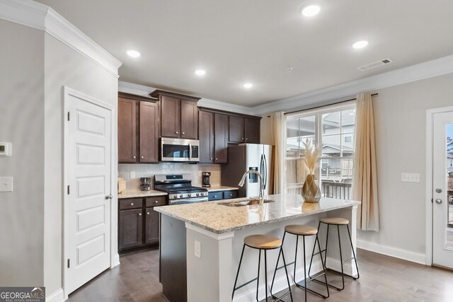 kitchen with pendant lighting, a kitchen breakfast bar, dark brown cabinetry, stainless steel appliances, and a center island with sink