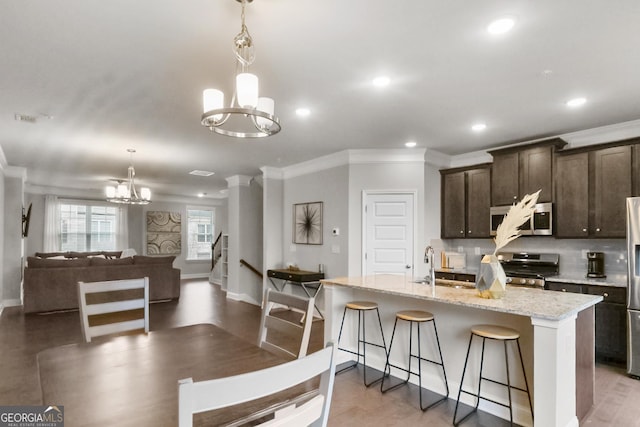 kitchen with an inviting chandelier, dark brown cabinets, stainless steel appliances, and an island with sink