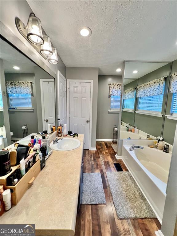 bathroom featuring toilet, a textured ceiling, vanity, a bathtub, and hardwood / wood-style floors