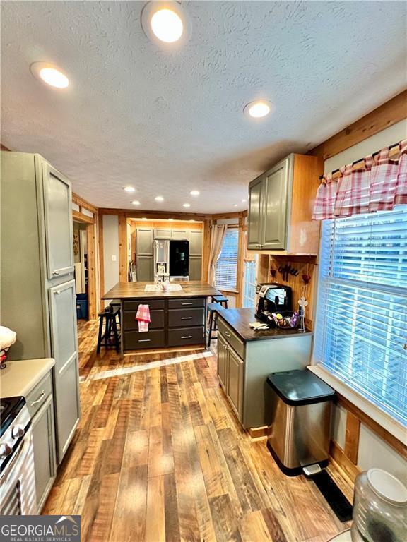 kitchen with fridge with ice dispenser, gray cabinetry, a textured ceiling, light hardwood / wood-style flooring, and a kitchen island