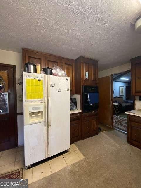 kitchen featuring light tile patterned floors, a textured ceiling, white refrigerator with ice dispenser, and black oven