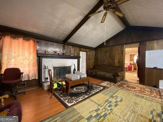 living area with lofted ceiling with beams, wooden walls, a fireplace, and a textured ceiling