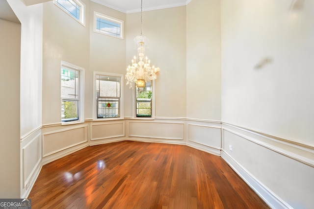 unfurnished dining area featuring crown molding, hardwood / wood-style floors, and a notable chandelier