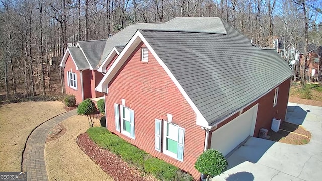 view of side of property with a shingled roof, concrete driveway, and brick siding