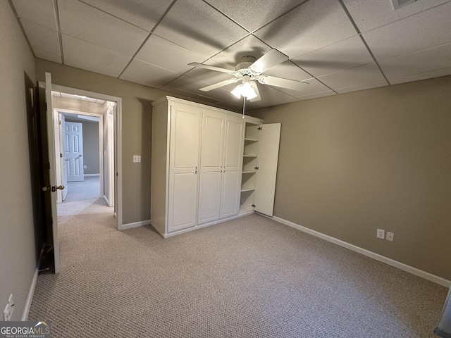 unfurnished bedroom featuring a closet, baseboards, a drop ceiling, and light colored carpet