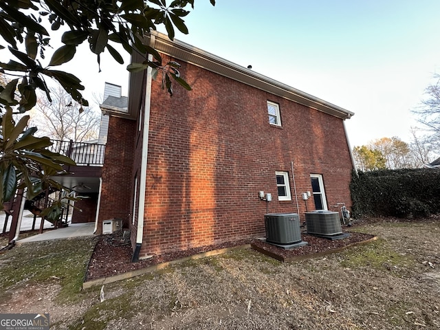 view of side of home with brick siding, a patio, and central AC unit