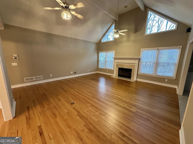 unfurnished living room featuring ceiling fan, a fireplace, wood finished floors, visible vents, and beam ceiling