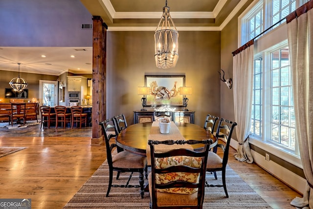 dining area with wood-type flooring, a wealth of natural light, ornamental molding, and a chandelier