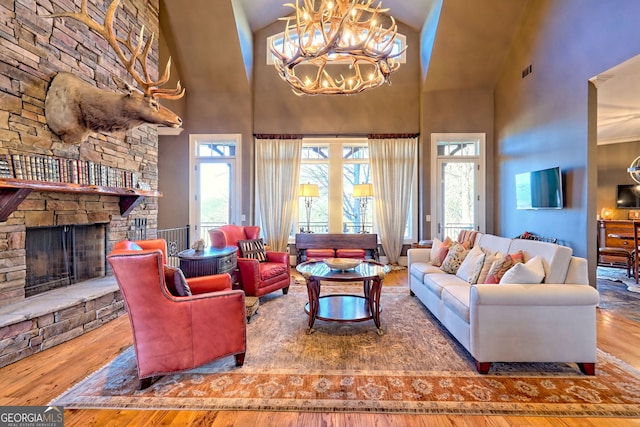 living room featuring wood-type flooring, a stone fireplace, a chandelier, and high vaulted ceiling