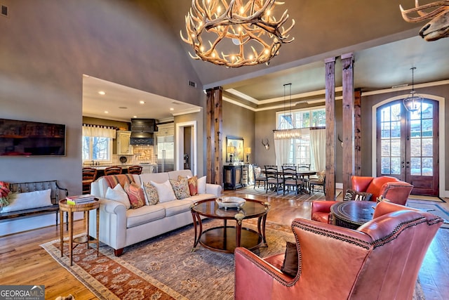 living room with decorative columns, ornamental molding, wood-type flooring, and high vaulted ceiling