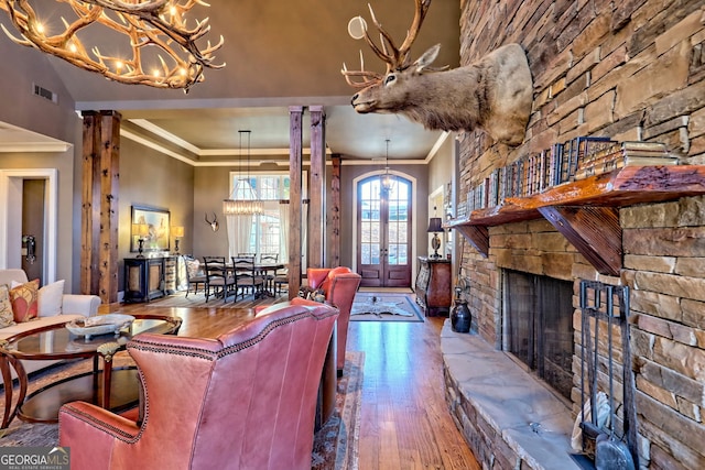 living room featuring ornate columns, an inviting chandelier, crown molding, wood-type flooring, and a fireplace