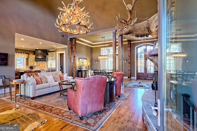 living room featuring ornate columns, wood-type flooring, a chandelier, a high ceiling, and ornamental molding