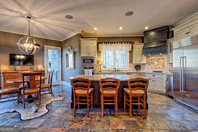 kitchen with a kitchen island, pendant lighting, a kitchen bar, built in appliances, and light stone countertops