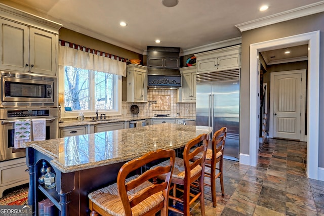 kitchen featuring sink, light stone counters, tasteful backsplash, built in appliances, and a kitchen island